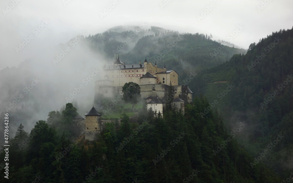 Fototapeta premium Old castle in the forest between mountains partly covered with fog