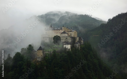 Old castle in the forest between mountains partly covered with fog 