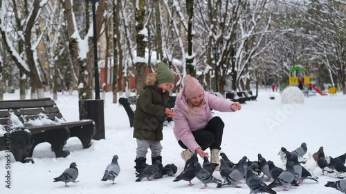 Little boy and mom are feeding pigeons. A child with his mother in a winter park throws bread to the birds on the snow. photo