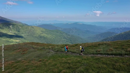 Two hikers with backpacks are walking along mountain range in Carpathian mountains.