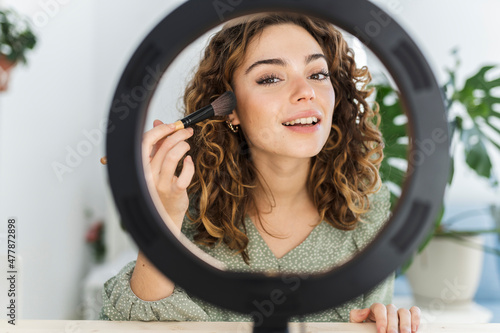 Foto pretty woman putting on makeup at home with light