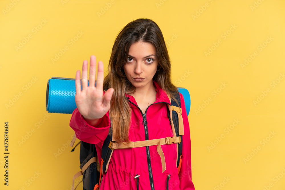Young mountaineer man with a big backpack isolated on yellow background making stop gesture Young mountaineer man with a big backpack isolated on yellow background making stop gesture