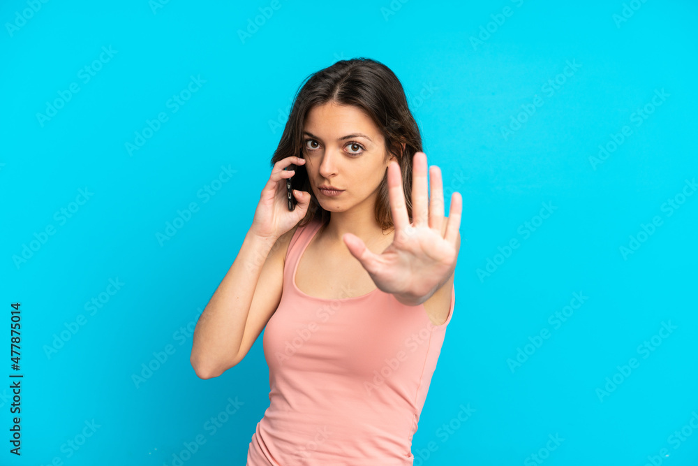 Young caucasian woman using mobile phone isolated on blue background making stop gesture Young caucasian woman using mobile phone isolated on blue background making stop gesture