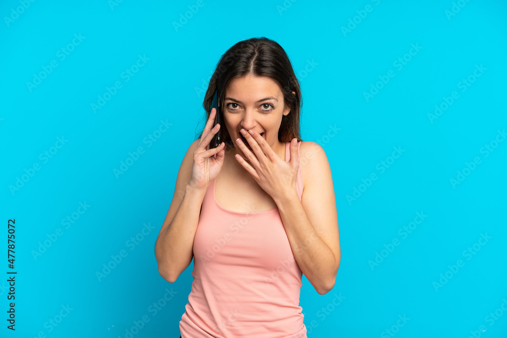 Young caucasian woman using mobile phone isolated on blue background happy and smiling covering mouth with hand Young caucasian woman using mobile phone isolated on blue background happy and smiling covering mouth with hand