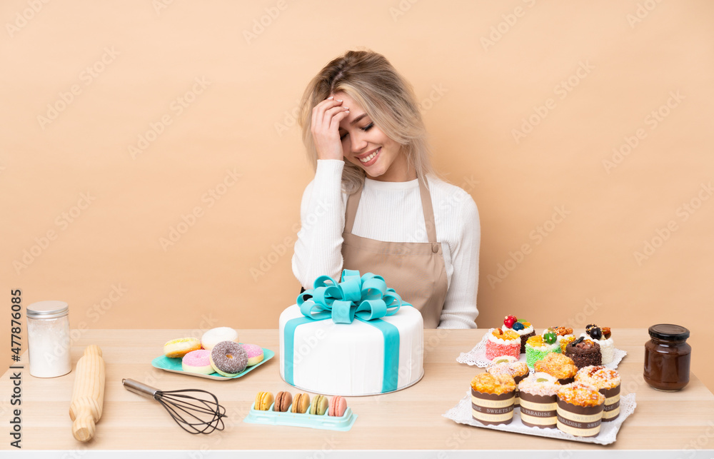 Teenager pastry chef with a big cake in a table laughing Teenager pastry chef with a big cake in a table laughing