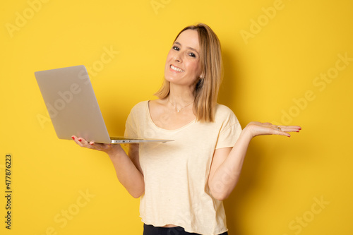 Young smiling woman in casual clothing with laptop computer isolated over yellow background.