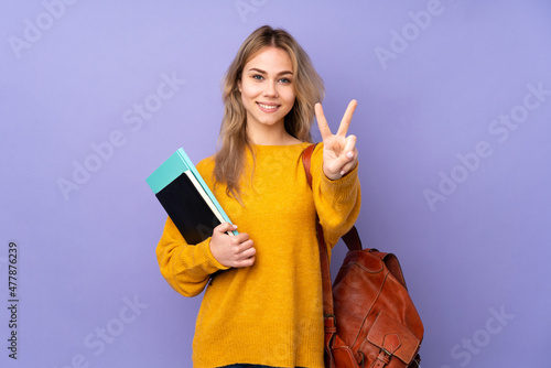Teenager Russian student girl isolated on purple background smiling and showing victory sign