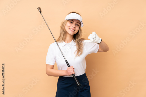 Teenager Russian girl isolated on beige background playing golf and proud of himself