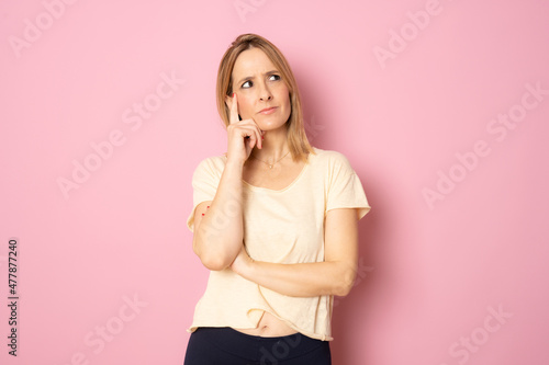 Young pensive woman in casual shirt standing isolated over pink background.