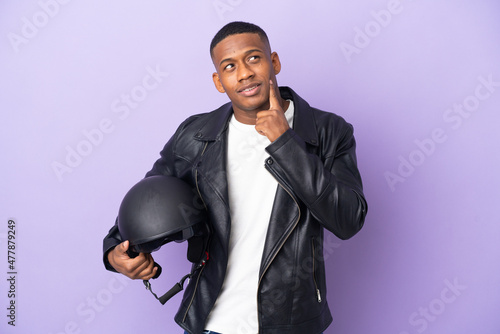 Latin man with a motorcycle helmet isolated on purple background thinking an idea while looking up