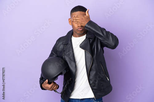 Latin man with a motorcycle helmet isolated on purple background covering eyes by hands. Do not want to see something