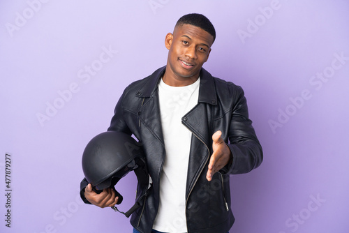 Latin man with a motorcycle helmet isolated on purple background shaking hands for closing a good deal