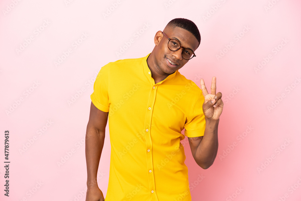 Young latin man isolated on pink background smiling and showing victory sign Young latin man isolated on pink background smiling and showing victory sign