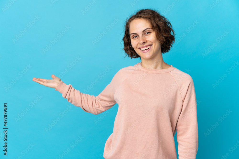 Young English woman isolated on blue background extending hands to the side for inviting to come Young English woman isolated on blue background extending hands to the side for inviting to come