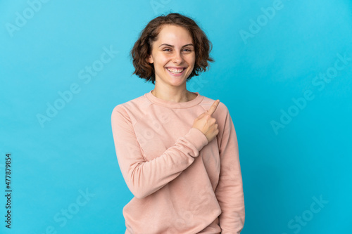 Young English woman isolated on blue background pointing to the side to present a product
