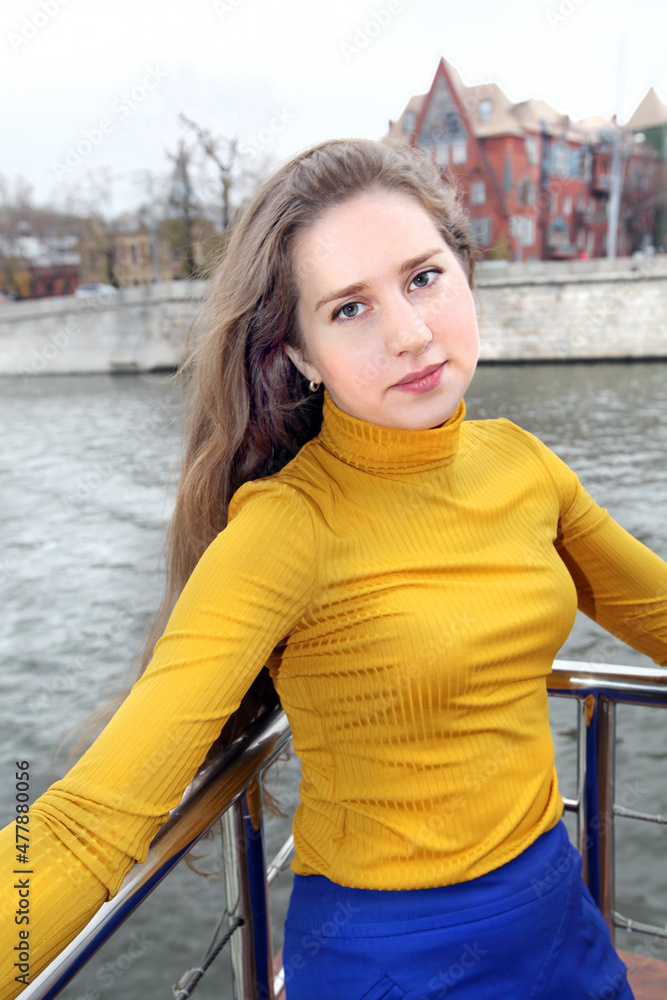 Portrait of a girl in a bright, yellow turtleneck on a gray river