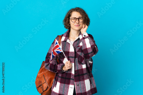 Young English woman holding an United Kingdom flag isolated on blue background frustrated and covering ears