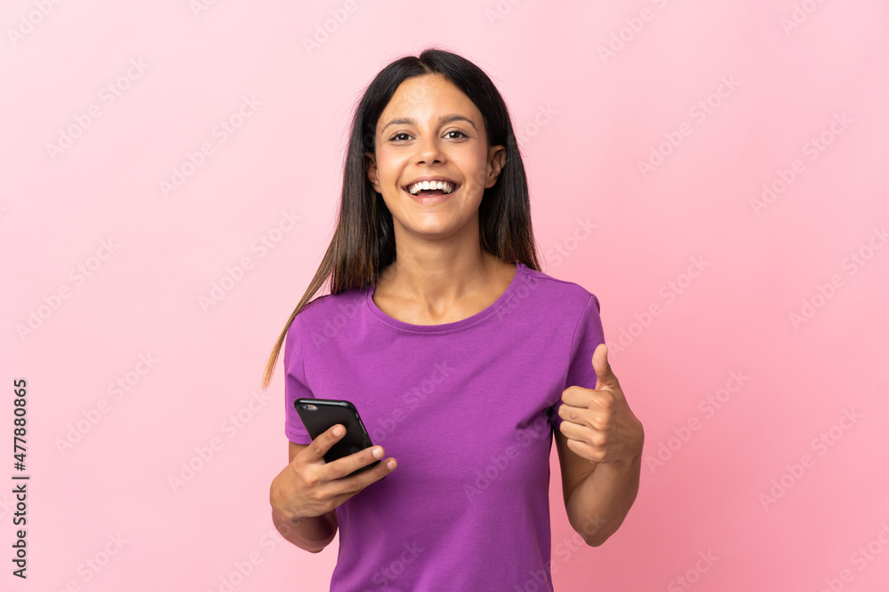 Caucasian girl isolated on pink background using mobile phone while doing thumbs up Caucasian girl isolated on pink background using mobile phone while doing thumbs up