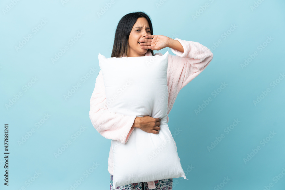 Young woman in pajamas over isolated background in pajamas and holding a pillow and yawning Young woman in pajamas over isolated background in pajamas and holding a pillow and yawning
