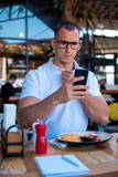 Businessman eating in a restaurant while using smartphone