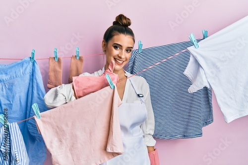 Beautiful brunette young woman washing clothes at clothesline doing happy thumbs up gesture with hand. approving expression looking at the camera showing success.