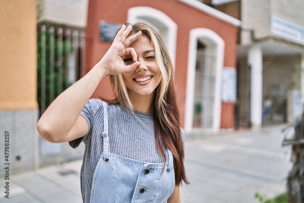 Young caucasian woman outdoors doing ok gesture with hand smiling, eye looking through fingers with happy face. Young caucasian woman outdoors doing ok gesture with hand smiling, eye looking through fingers with happy face.