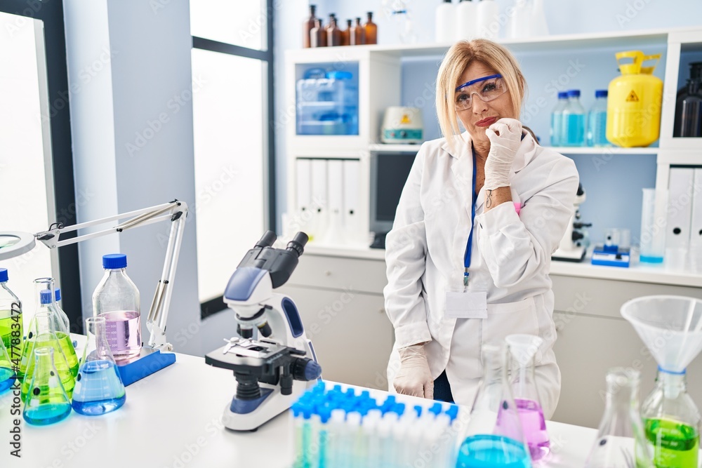 Middle age blonde woman working at scientist laboratory looking stressed and nervous with hands on mouth biting nails. anxiety problem. Middle age blonde woman working at scientist laboratory looking stressed and nervous with hands on mouth biting nails. anxiety problem.