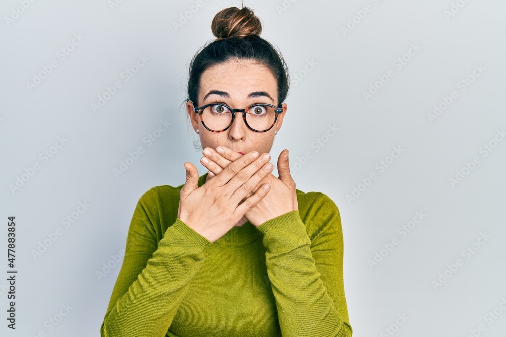 Young hispanic girl wearing casual clothes and glasses shocked covering mouth with hands for mistake. secret concept. Young hispanic girl wearing casual clothes and glasses shocked covering mouth with hands for mistake. secret concept.