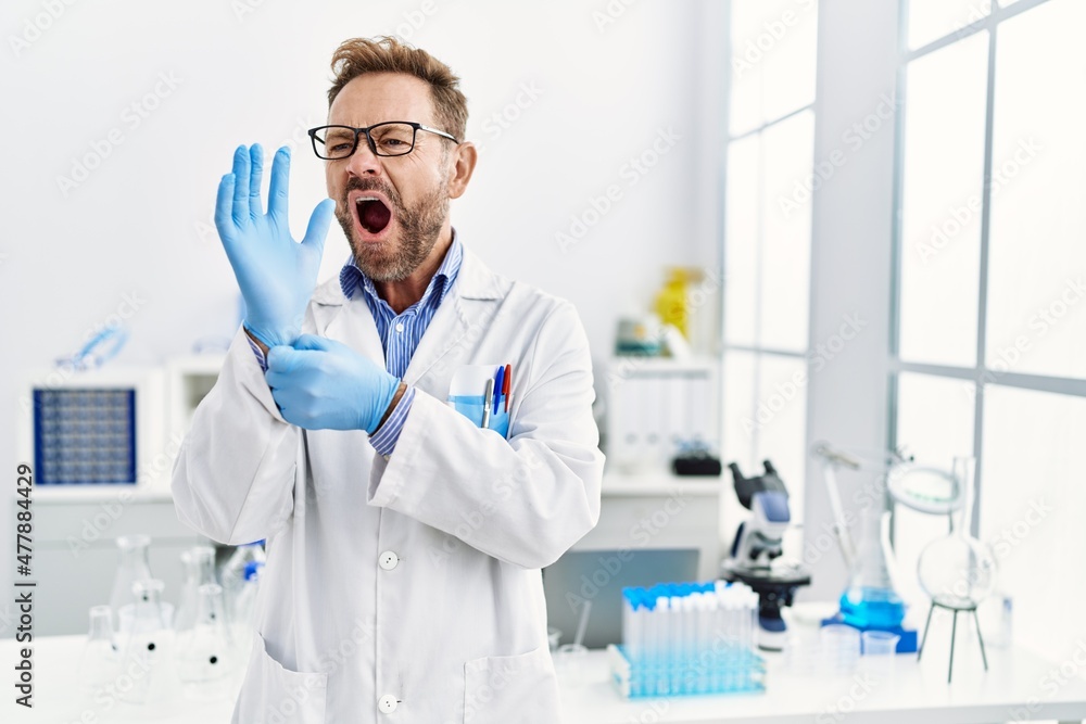 Middle age man working at scientist laboratory angry and mad screaming frustrated and furious, shouting with anger. rage and aggressive concept.