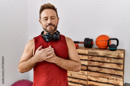 Middle age man wearing sportswear and headphones at the gym smiling with hands on chest with closed eyes and grateful gesture on face. health concept. © Krakenimages.com