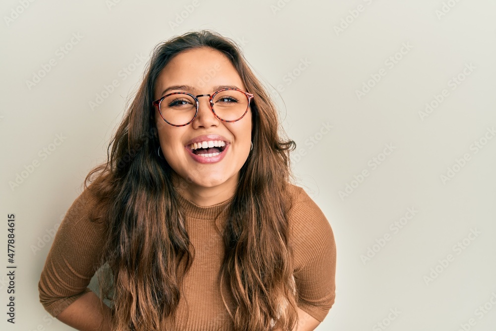 Young hispanic girl wearing casual clothes and glasses smiling and laughing hard out loud because funny crazy joke with hands on body. Young hispanic girl wearing casual clothes and glasses smiling and laughing hard out loud because funny crazy joke with hands on body.