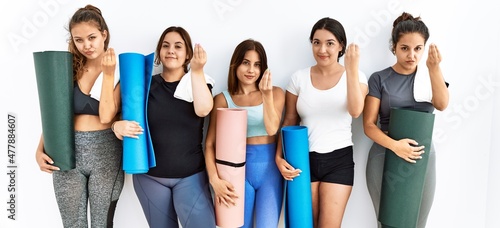 Group of women holding yoga mat standing over isolated background doing italian gesture with hand and fingers confident expression