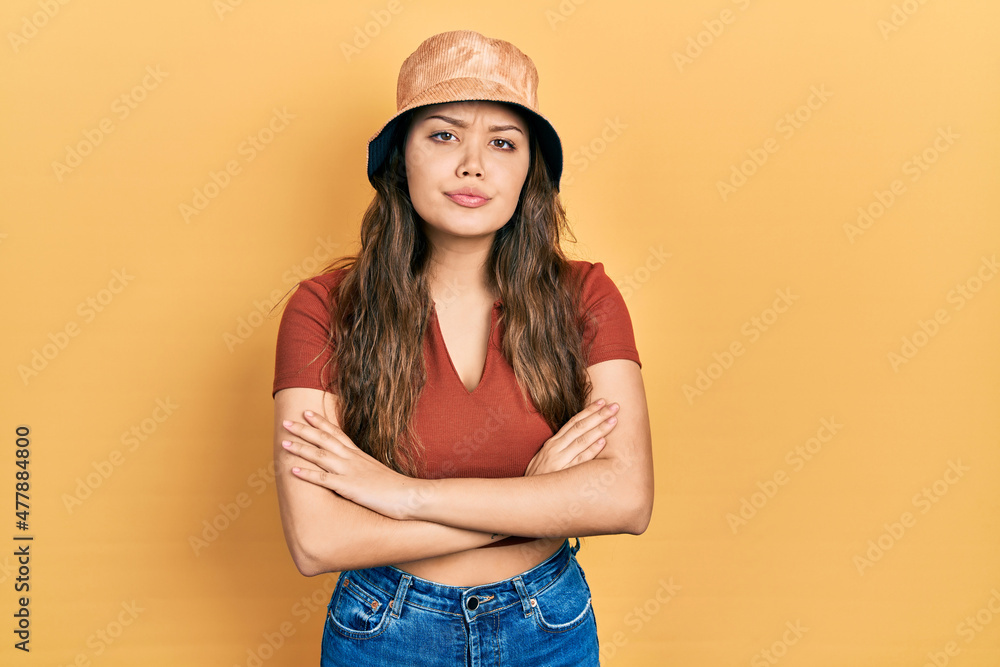 Young hispanic girl wearing casual clothes and hat skeptic and nervous, disapproving expression on face with crossed arms. negative person. Young hispanic girl wearing casual clothes and hat skeptic and nervous, disapproving expression on face with crossed arms. negative person.