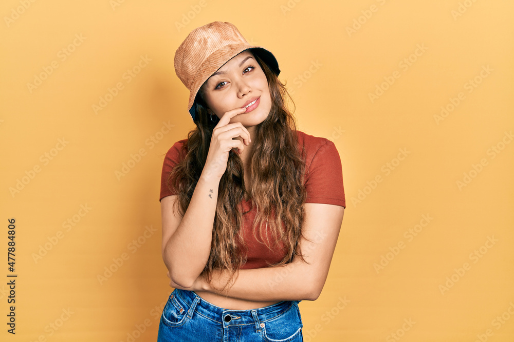 Young hispanic girl wearing casual clothes and hat looking confident at the camera with smile with crossed arms and hand raised on chin. thinking positive. Young hispanic girl wearing casual clothes and hat looking confident at the camera with smile with crossed arms and hand raised on chin. thinking positive.