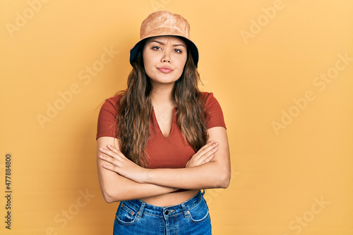 Young hispanic girl wearing casual clothes and hat skeptic and nervous, disapproving expression on face with crossed arms. negative person.