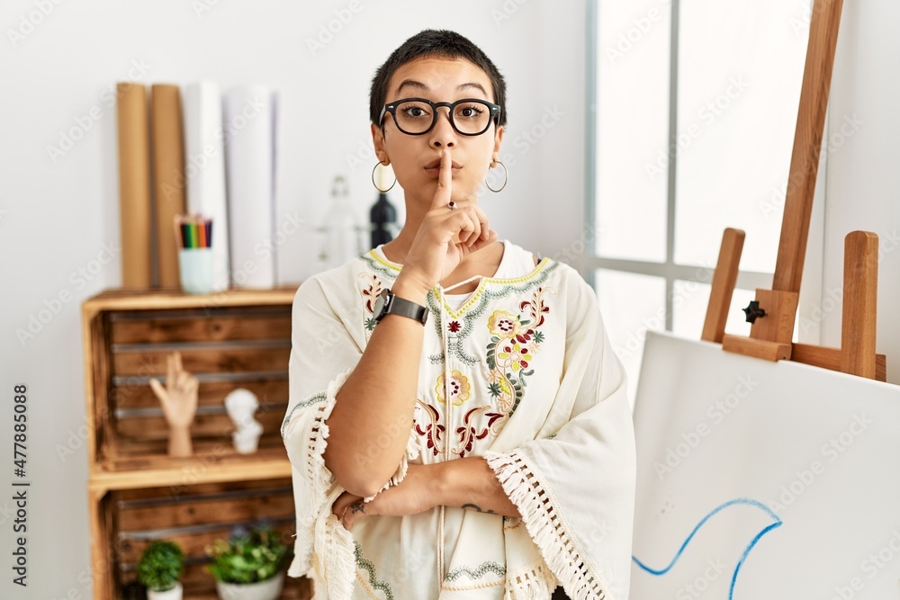 Young hispanic woman with short hair at art studio asking to be quiet with finger on lips. silence and secret concept. Young hispanic woman with short hair at art studio asking to be quiet with finger on lips. silence and secret concept.