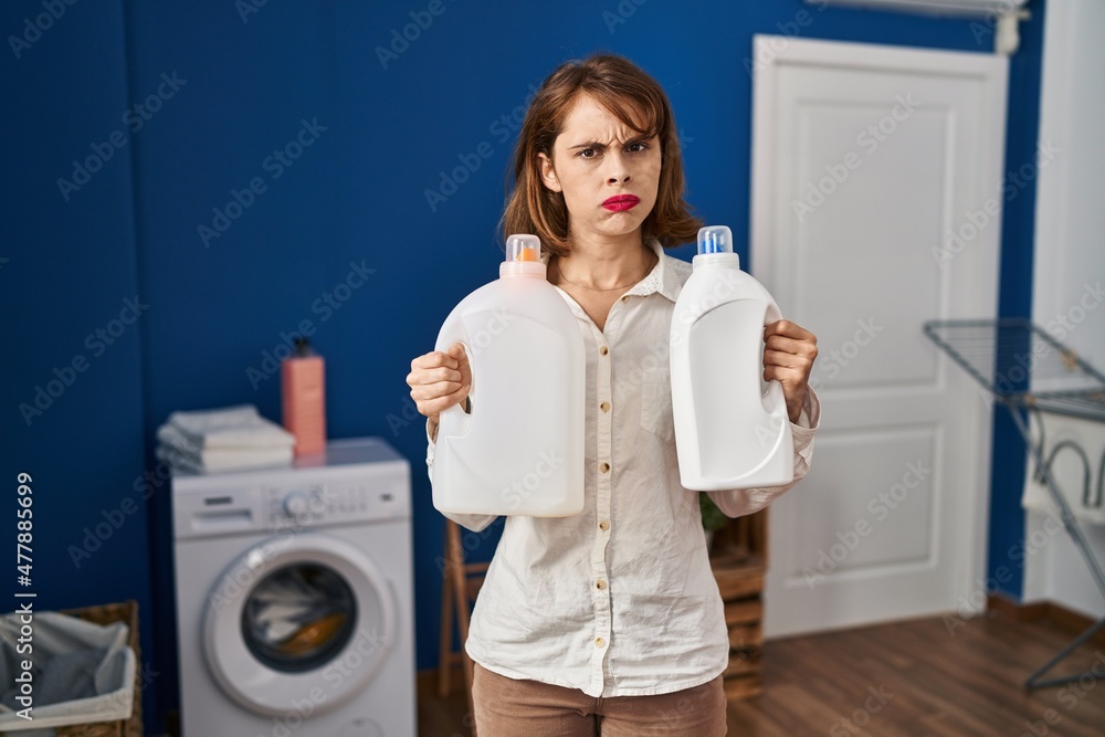 Young beautiful woman holding detergent bottles skeptic and nervous, frowning upset because of problem. negative person. Young beautiful woman holding detergent bottles skeptic and nervous, frowning upset because of problem. negative person.