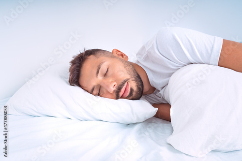 Handsome cute man sleeping in the bed with white beddings. Man lying on the pillow and enjoying good healthy sleep