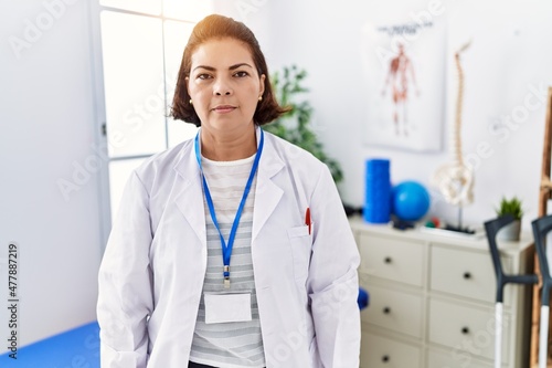 Middle age hispanic woman working at pain recovery clinic with serious expression on face. simple and natural looking at the camera.