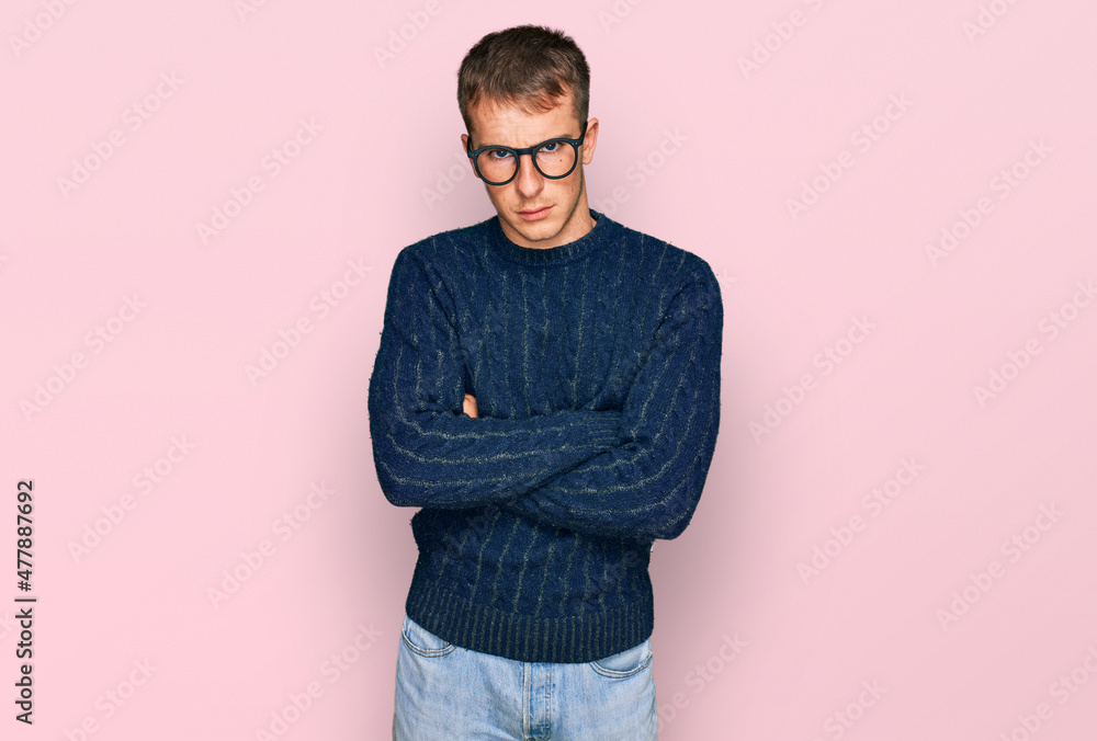 Young blond man wearing casual clothes and glasses skeptic and nervous, disapproving expression on face with crossed arms. negative person. Young blond man wearing casual clothes and glasses skeptic and nervous, disapproving expression on face with crossed arms. negative person.