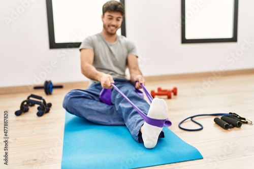 Young hispanic sporty man smiling happy training using elastic band at sport center.