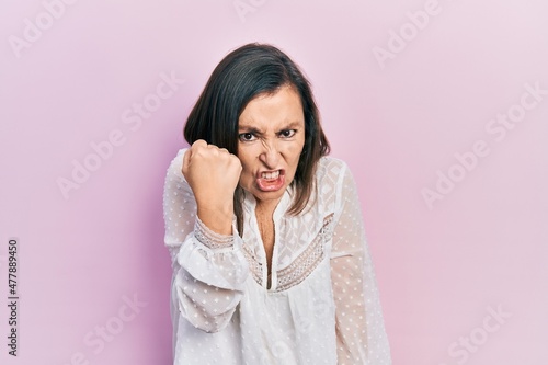 Middle age hispanic woman wearing casual clothes angry and mad raising fist frustrated and furious while shouting with anger. rage and aggressive concept. © Krakenimages.com