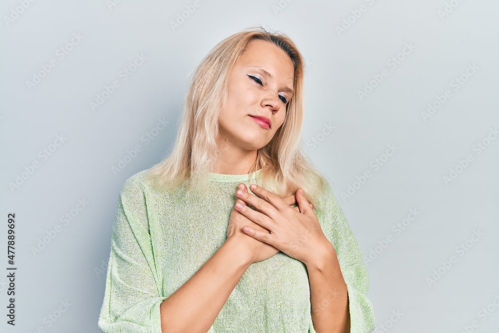 Beautiful caucasian blonde woman wearing casual winter sweater smiling with hands on chest, eyes closed with grateful gesture on face. health concept. Beautiful caucasian blonde woman wearing casual winter sweater smiling with hands on chest, eyes closed with grateful gesture on face. health concept.