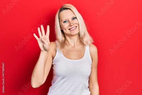 Beautiful caucasian blonde woman wearing casual white t shirt showing and pointing up with fingers number four while smiling confident and happy.