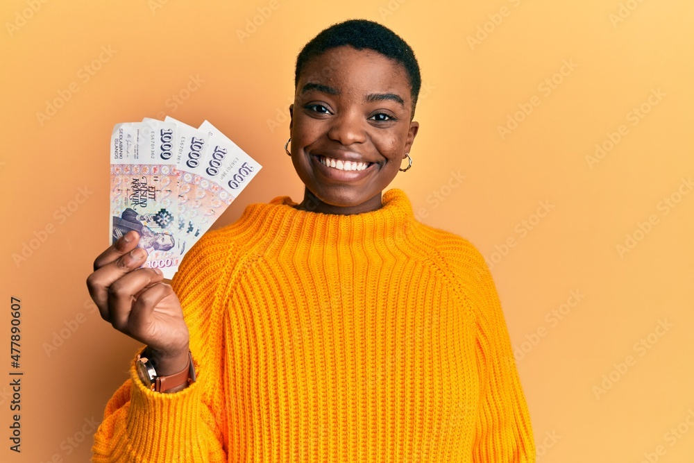 Young african american woman holding icelandic krona banknotes looking positive and happy standing and smiling with a confident smile showing teeth Young african american woman holding icelandic krona banknotes looking positive and happy standing and smiling with a confident smile showing teeth