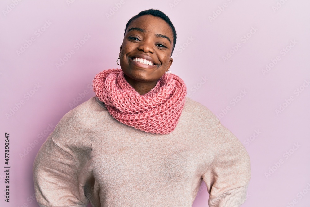 Young african american woman wearing winter scarf looking positive and happy standing and smiling with a confident smile showing teeth Young african american woman wearing winter scarf looking positive and happy standing and smiling with a confident smile showing teeth