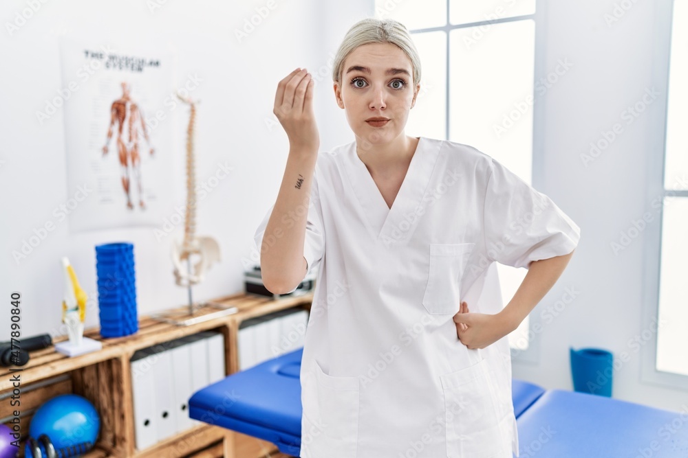 Young caucasian woman working at pain recovery clinic doing italian gesture with hand and fingers confident expression Young caucasian woman working at pain recovery clinic doing italian gesture with hand and fingers confident expression