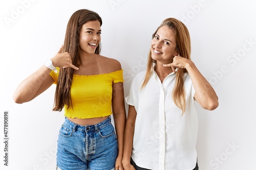Mother and daughter together standing together over isolated background smiling doing phone gesture with hand and fingers like talking on the telephone. communicating concepts.