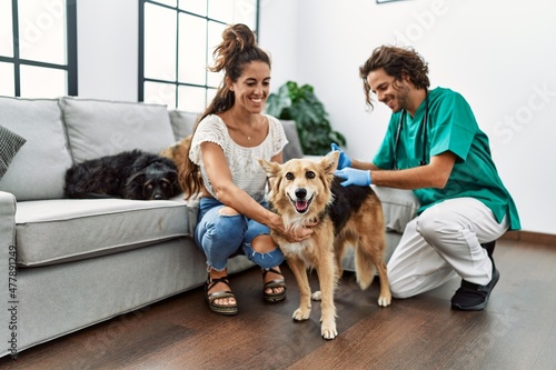 Quadro em tela Man and woman wearing veterinarian uniform injecting vaccine to dog at home