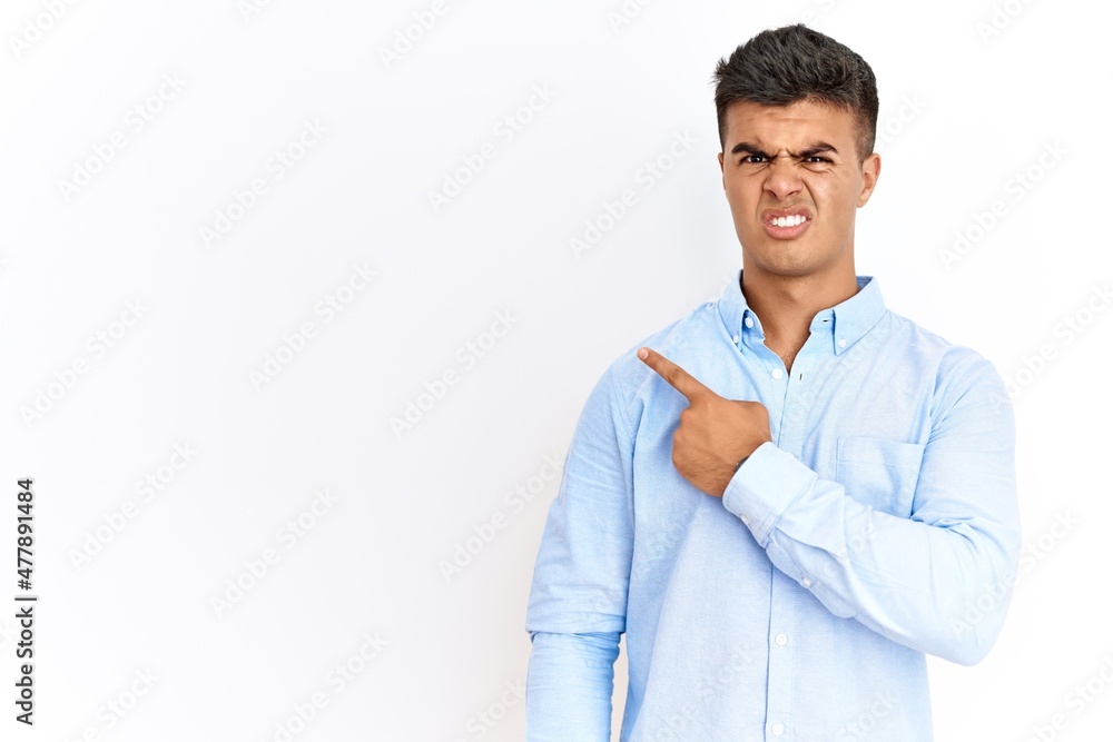 Young hispanic man wearing business shirt standing over isolated background pointing aside worried and nervous with forefinger, concerned and surprised expression Young hispanic man wearing business shirt standing over isolated background pointing aside worried and nervous with forefinger, concerned and surprised expression